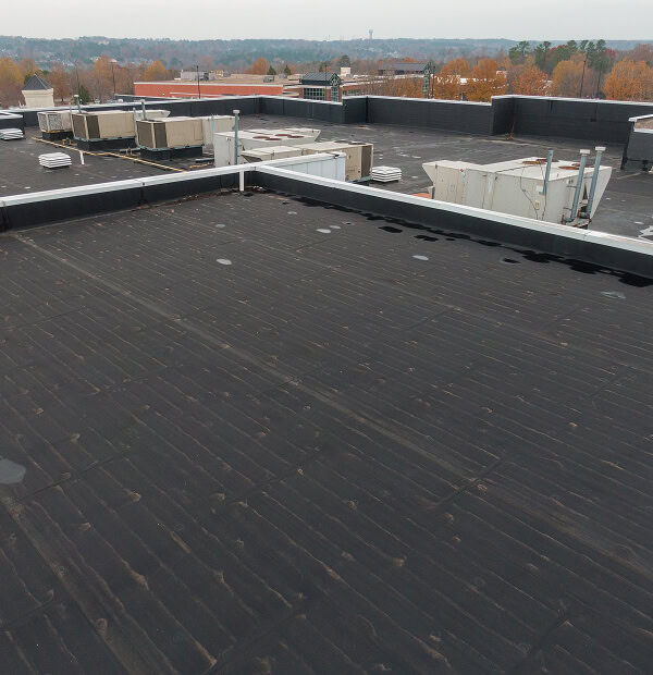 Flat commercial roof with HVAC units, dark membrane, and landscape, ideal for storm damage restoration and large-loss recovery.