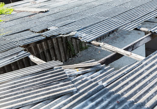 Commercial roofing with storm damage: large hole, bent panels needing large-loss restoration.