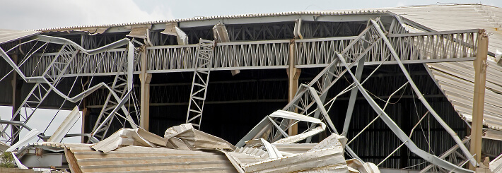 Collapsed commercial warehouse with bent beams and panels after severe storm damage, showing need for large-loss restoration and reroofing.