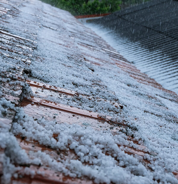 Hailstones cover a sloped commercial roof, showing storm damage restoration needs.