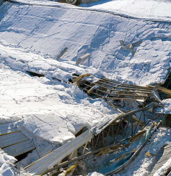 Commercial flat roof collapsed under heavy snow, with broken beams—large-loss restoration needed.