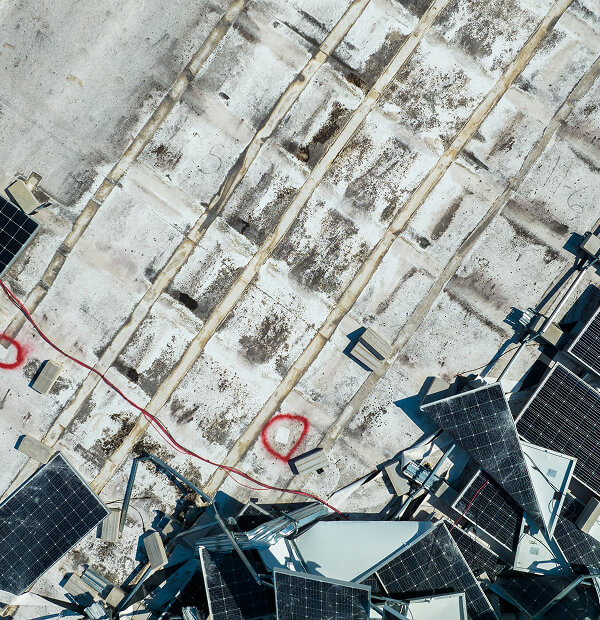 Aerial view of a flat commercial roof with solar panels and red storm damage markings.