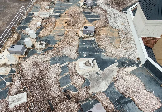 Flat commercial roof with gravel, exposed patches, HVAC units, and storm damage restoration needs.
