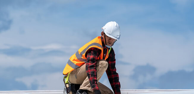A commercial roofer in safety gear kneels on a flat roof for large-loss restoration.