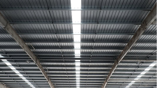 Interior view of commercial roofing with corrugated metal panels, skylight strip, and reinforced beams for large-loss recovery.