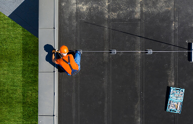 A worker in safety gear on a commercial flat roof with tools, handling large-loss storm damage restoration.