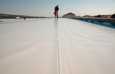A worker inspects a commercial flat roof for storm damage restoration and large-loss recovery.