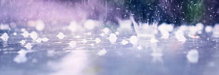 Close-up of raindrops on a wet flat commercial roof, with blurred colors in the background, symbolizing storm damage restoration.