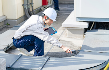 A commercial roofing inspector in a white helmet checks flat roof equipment for storm damage restoration.