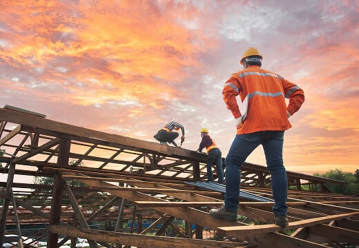 Commercial roofing crew in safety gear assembles steel flat roof frame at sunset for large-loss storm damage restoration.