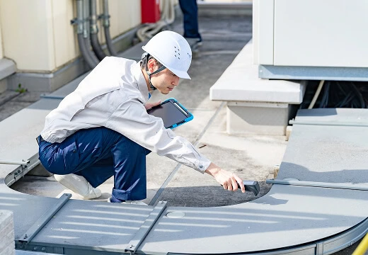 A commercial roofing inspector assesses flat roof equipment with a tablet for large-loss recovery.