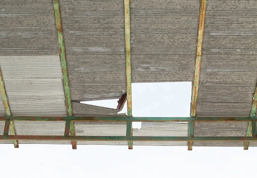 Commercial roofing with a large hole, rusted beams, and storm damage restoration needs.