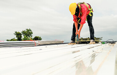 A worker in a yellow hard hat installs metal sheets on a commercial roof for large-loss storm damage restoration.