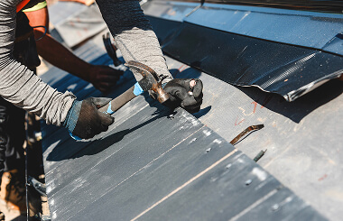 A worker in gloves hammers metal panels during commercial roofing and large-loss restoration.