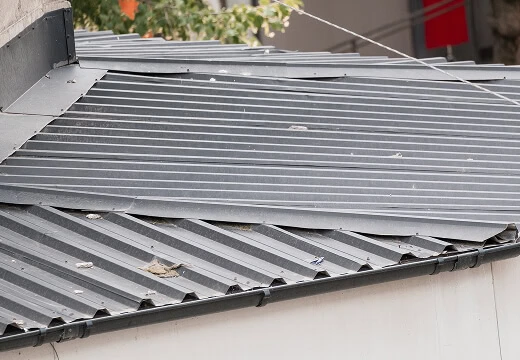 Corrugated metal commercial roofing with debris, showing storm damage restoration needs.