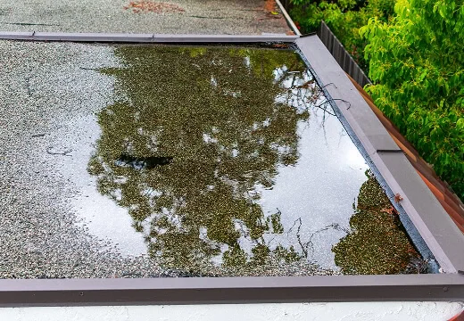Water pooling on a flat commercial roof, gravel-covered, with storm damage reflection.
