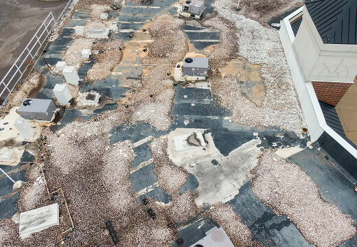 Flat commercial roof with exposed membrane, gravel, HVAC units, and storm damage for large-loss restoration.