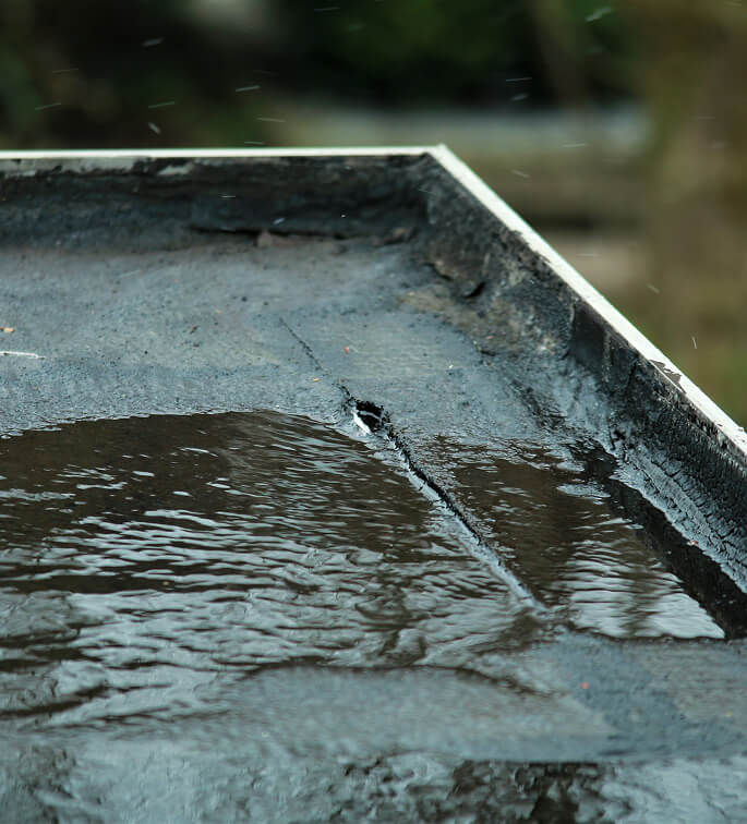 Close-up of commercial flat roof with pooling water, cracks, and signs of large-loss storm damage restoration needed.