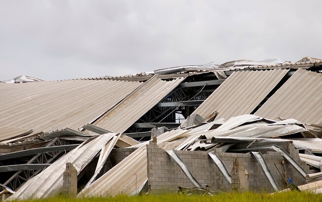 Collapsed commercial building with flat metal roof, debris, and storm damage restoration underway.