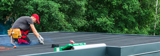 A commercial roofer applies materials to a flat roof for large-loss storm restoration.