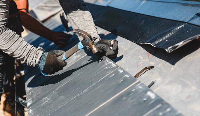 Commercial roofing technician in gloves repairing metal flat roof after storm damage.
