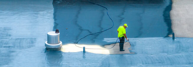 A worker in neon yellow uses equipment on a commercial flat roof for large-loss restoration.