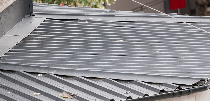Close-up of commercial metal roof panels showing dirt, debris, and storm damage for large-loss restoration.