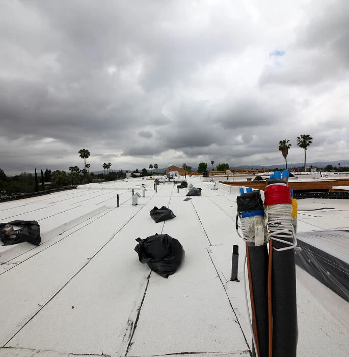 Flat commercial roof with storm damage restoration materials, vents, and palm trees in background.