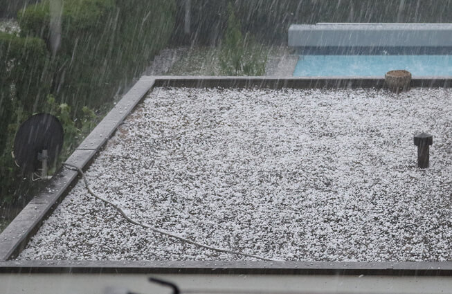 Hailstones cover a commercial flat roof during a storm, highlighting storm damage restoration and large-loss recovery needs.